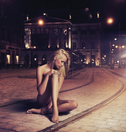 Naked young woman in sensual pose on the street