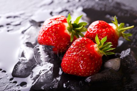 Three fresh red strawberries on slate stone with ice