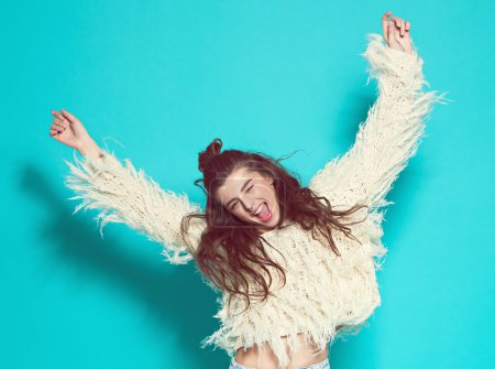 portrait of cheerful fashion hipster girl going crazy making funny face and dancing. Blue color background.