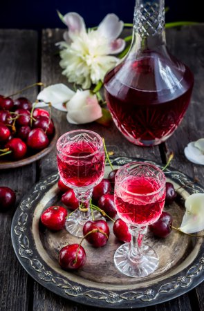 Cherry  liquor in glasses, cherry  and vintage bottle on metal tray.