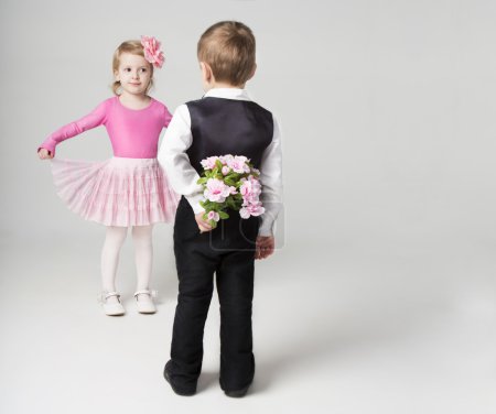 Boy hiding behind a flowers. Going to give a girl a bouquet. Girl is flirting. Studio shot. Gray background. Sweet relationship.