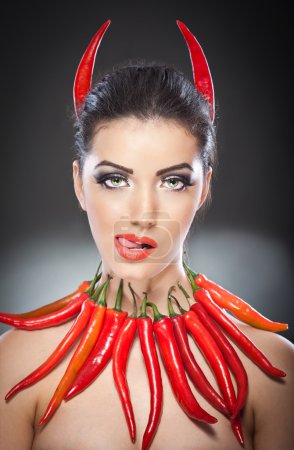 beautiful young woman portrait with red hot and spicy peppers, fashion model with creative food vegetable make up looking side to empty copy space, isolated over black background. Red chili Paprika.