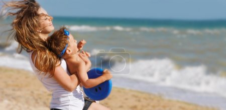 young happy mother playing with son on beach background