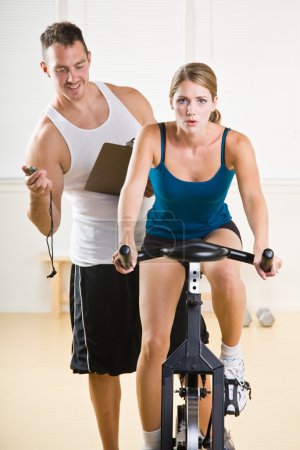 Trainer timing woman on stationary bicycle