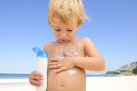 Cute child applying sunscreen at the beach