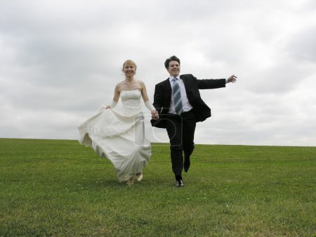 Bride and groom running on meadow