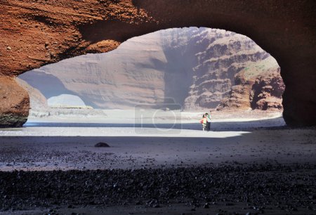 Young couple walking under arch rock formation near Atlantic in Morocco