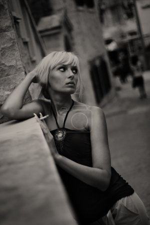 Portrait of young woman smoking cigarette in old city street background.