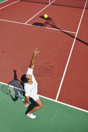 Young man play tennis outdoor on orange tennis court at early morning