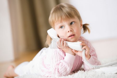 Little girl lying down on carpet with phone calling holding telephone receiver at home