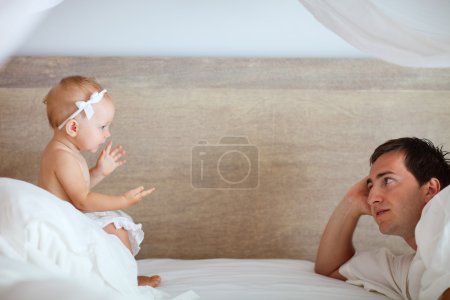 Young father and cute baby girl talking with each other in bed