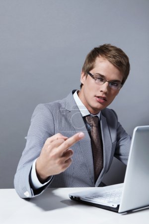 Young attractive man in a suit with the laptop shows an obscene sign to the camera