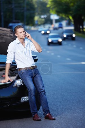 The young man next to a smashed car on the phone