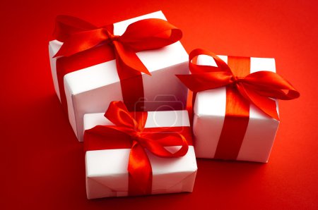 Small white gift boxes with red ribbon over red background. Use it for special events illustrations.