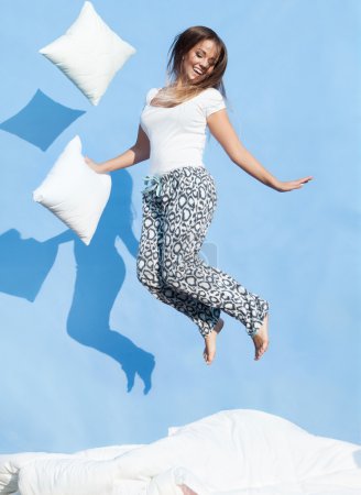 Woman holding a pillow jumping up on bed
