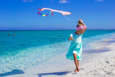 Little happy girl playing with flying kite on tropical beach
