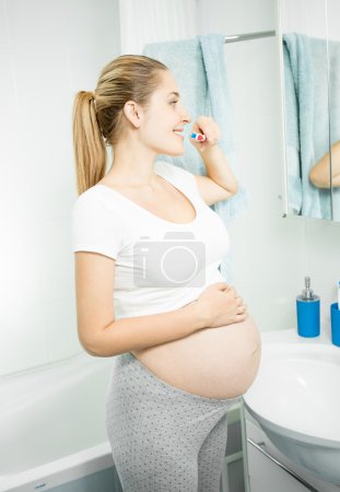 beautiful pregnant woman brushing teeth at bathroom