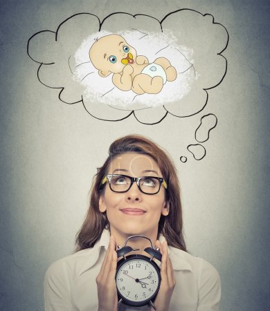 woman anticipating a baby looking up holding alarm clock