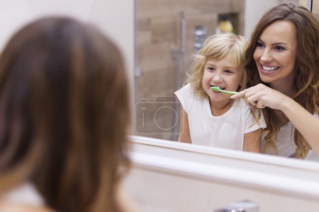 Mother teaches daughter to brush teeth