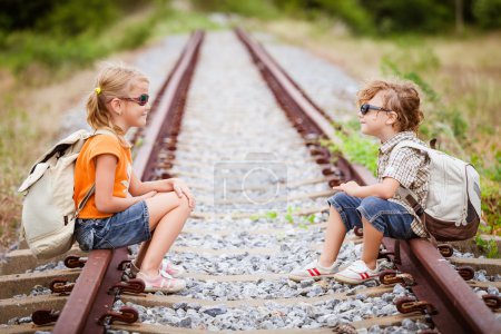 two little kids with backpack sitting on the railway