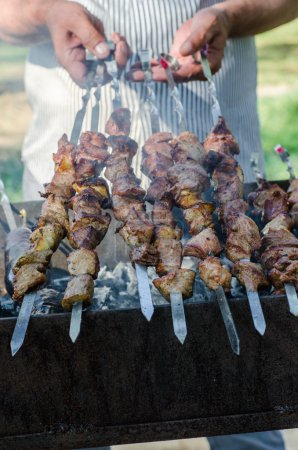 Man cooking marinated shashlik or shish kebab, chiken meat grilling on metal skewer, close up. Selective focus