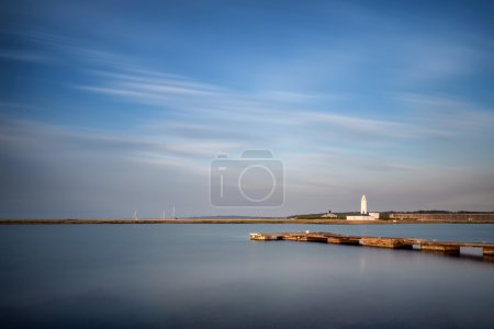 Landscape long exposure of lighthouse and jetty during Summer su