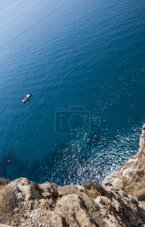 Top view of a deep blue sea and rocks of the coast. A little boa