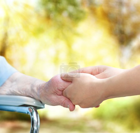 Senior lady in wheel chair holding hands with young caretaker