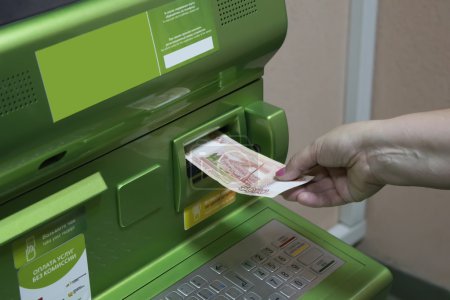 A man (woman) puts a banknotes into a slot of the ATM.