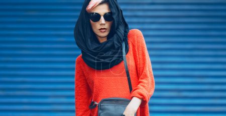 Fashion girl portrait in a stylish black headscarf and sunglasses on a blue background. Urban style