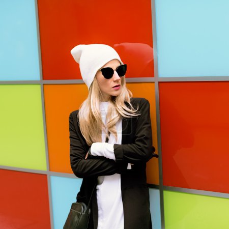 Fashionable blonde standing against a bright wall. Urban autumn 