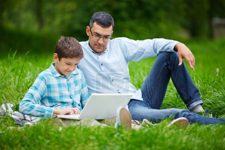 Man and son using laptop  in  park