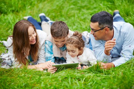 Family lying on grass with touchpad