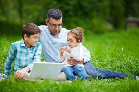 Man and two children using laptop in park