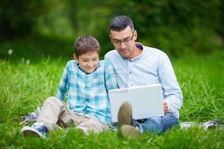 Father and son using laptop in park