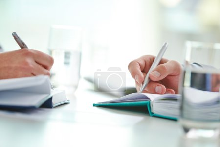 Male and female hands writing  in notebooks