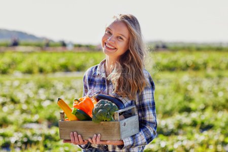 Young woman holding wooden crate with vegetables