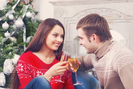 Young happy couple drinking champagne by the Cristmas tree