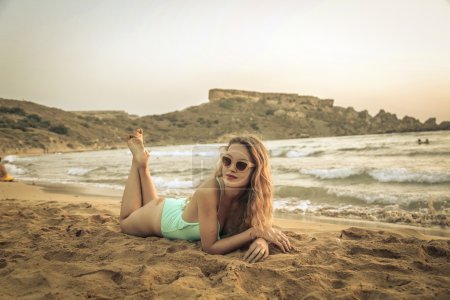 Beautiful blonde girl lying in the sand at sunset