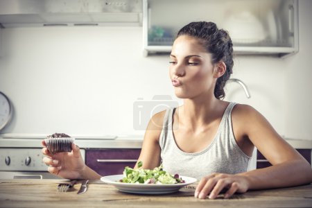 Young girl deciding whether to eat a healty salad or a muffin