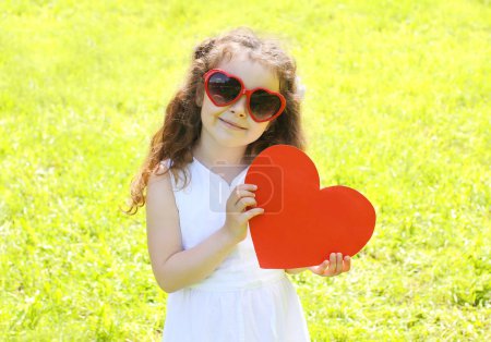 Little girl child in sunglasses with big red paper heart over su
