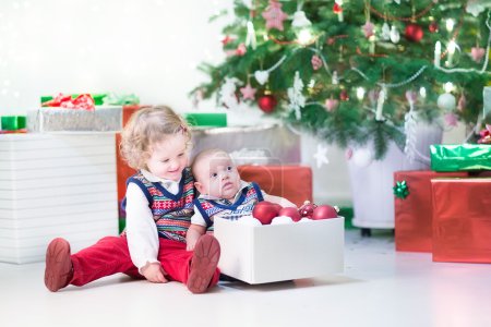 Little toddler girl and her newborn brother helping to decorate new year tree