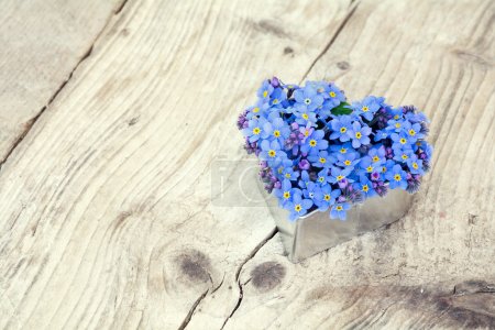 Heart shape with forget-me-not flowers on  rustic wood