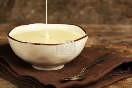 Bowl with condensed milk on napkin on wooden background
