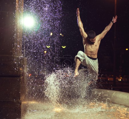 Muscular man jumping in fountain