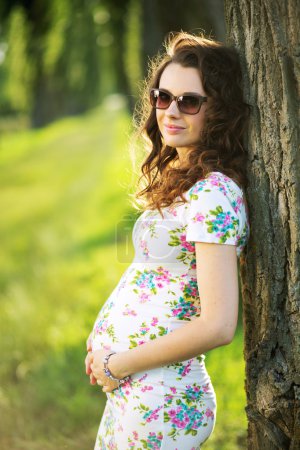Marvelous pregnant woman leaning against the tree
