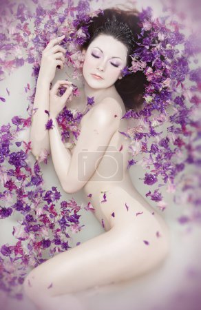 Attractive naked girl enjoys a bath with milk and rose petals. Spa treatmen
