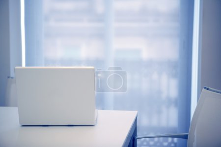White laptop open on a white room, blue light