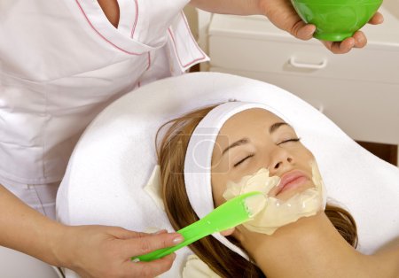 Young woman getting beauty skin mask treatment on her face with