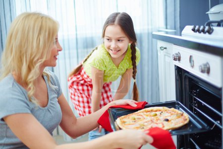 Woman taking pizza out of oven